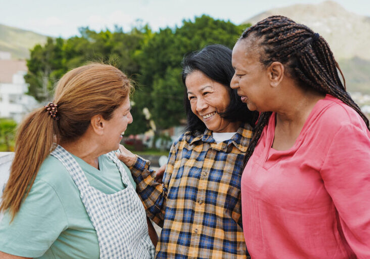 Happy multiracial senior women having fun together outdoor - Elderly generation people hugging each other at home terrace